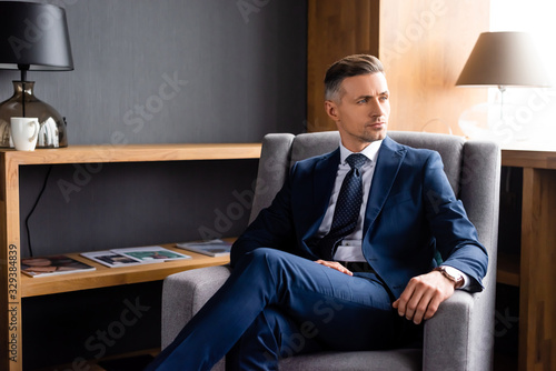 Canvas Print handsome businessman in suit sitting in armchair and looking away