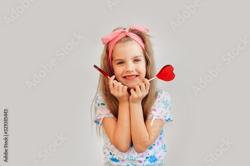 Portrait of a beautiful stylish fashionable girl in glasses, with a heart-shaped lollipop, on a white background, free time summer vacation #329385443