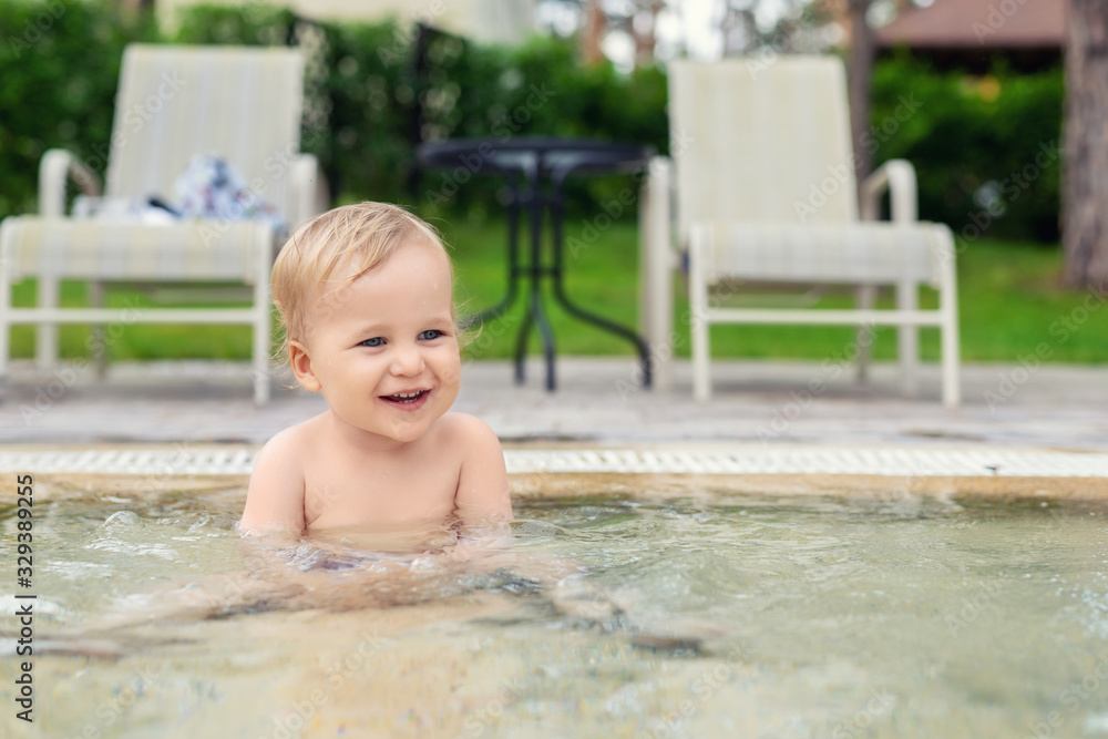 Happy little caucasian blond toddler boy swimming in wading pool on bright summer day at resort. Adorable baby enjoying outdoor water fun activities in shallow water. Children travel and holidays Happy little caucasian blond toddler boy swimming in wading pool on bright summer day at resort. Adorable baby enjoying outdoor water fun activities in shallow water. Children travel and holidays