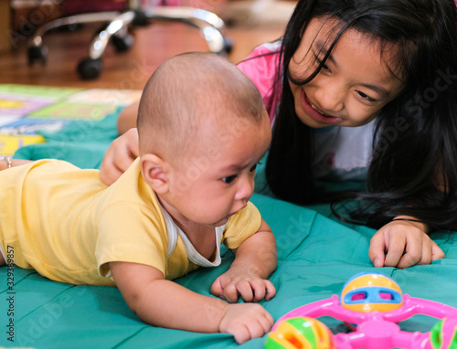 caucasian girl black long hair smile with baby boy and playing fun. sibling love in thailand family