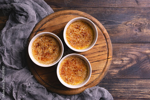 Photos Homemade creme brulee - traditional french vanilla cream dessert with caramelised brown sugar on top, wooden plate and table