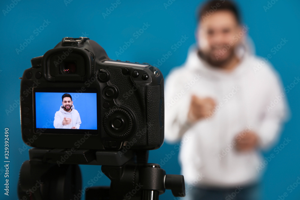 Young blogger shooting video with camera against blue background, focus on screen