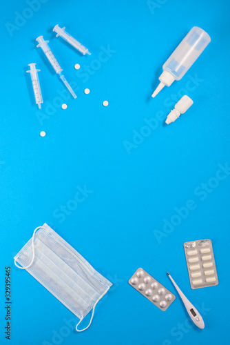 Syringes, pills, thermometer, mask and drops on a blue background. Vertical orientation, top view, copy space. photo