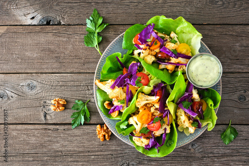 Healthy lettuce wraps with grilled cauliflower, cabbage and tomatoes. Above view over a rustic wood background. Plant-based diet concept. photo