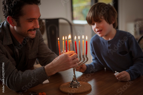 Boy looking at smiling father burning candles on menorah during Hanukkah festival
