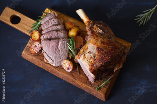 Roast leg of lamb with potatoes and rosemary on serving wooden board. View from above, top view