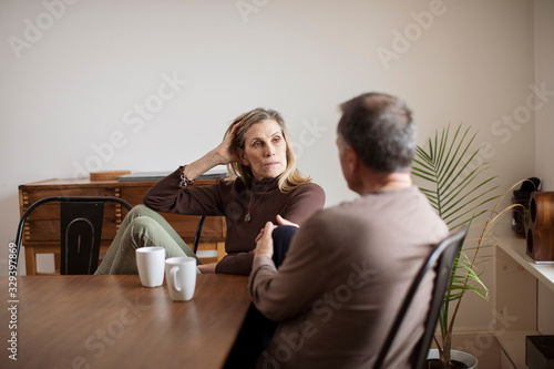 Obraz na plátně Senior woman listening to man while having coffee at table in living room