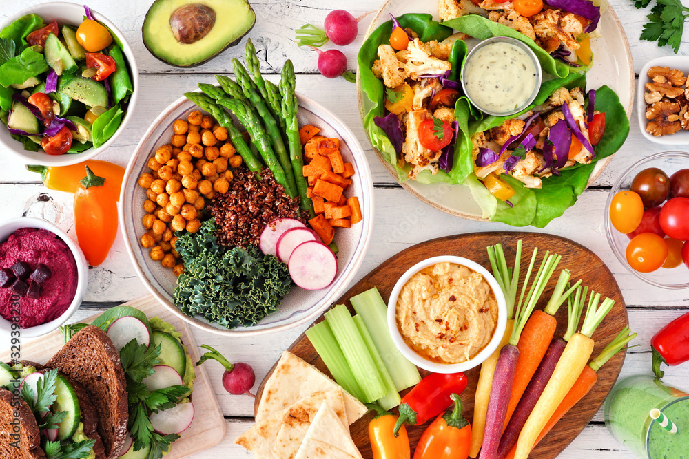 Healthy lunch table scene with nutritious Buddha bowl, lettuce wraps, vegetables, sandwiches and salad. Top view over a white wood background. Healthy lunch table scene with nutritious Buddha bowl, lettuce wraps, vegetables, sandwiches and salad. Top view over a white wood background.
