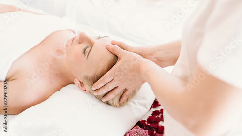 Beautiful caucasian woman having a facial massage treatment in spa salon with the hands of a therapist as a foreground  selective focus  concept spa and beauty  facial spa treatment  esthetic spa.