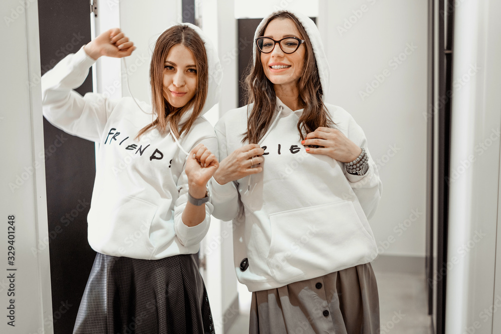 Shopping, fitting clothes. Two girls in a fitting room in identical white clothes. Fun and joy of consumption. LGBT and lesbians. Female friendship and leisure. Shopping, fitting clothes. Two girls in a fitting room in identical white clothes. Fun and joy of consumption. LGBT and lesbians. Female friendship and leisure.