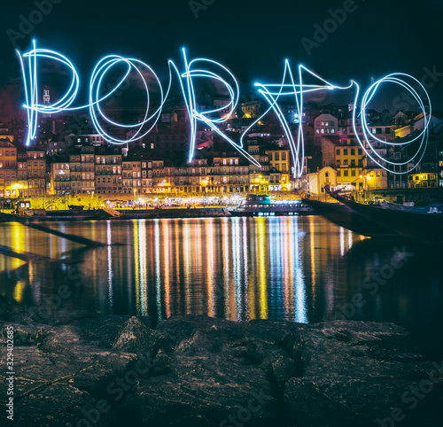 Porto, Portugal old town skyline at night on the Douro River with the word "Oporto" written with light painting.