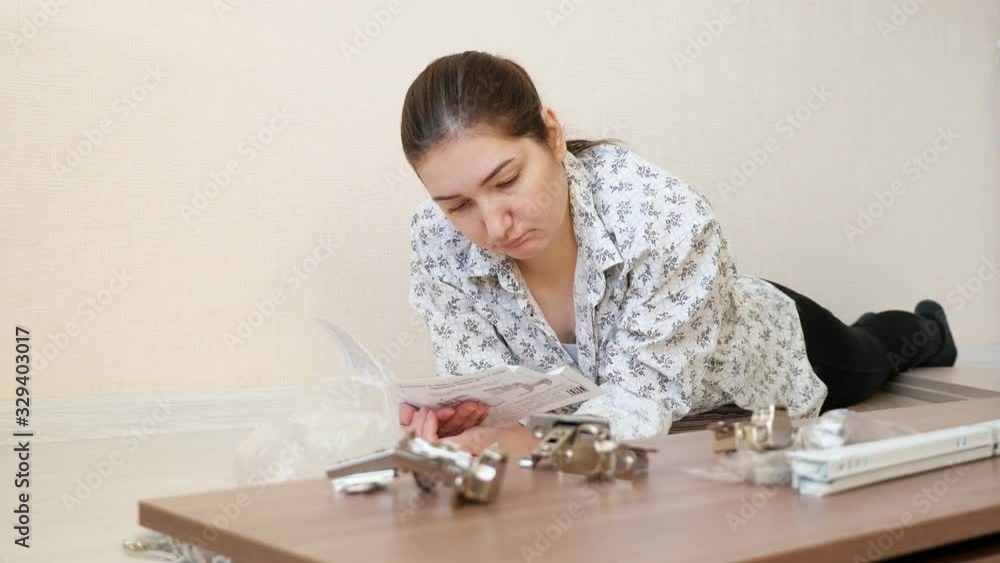 serious woman with ponytail lies on floor and reads instruction for assembling kitchen cabinet close-up serious woman with ponytail lies on floor and reads instruction for assembling kitchen cabinet close-up