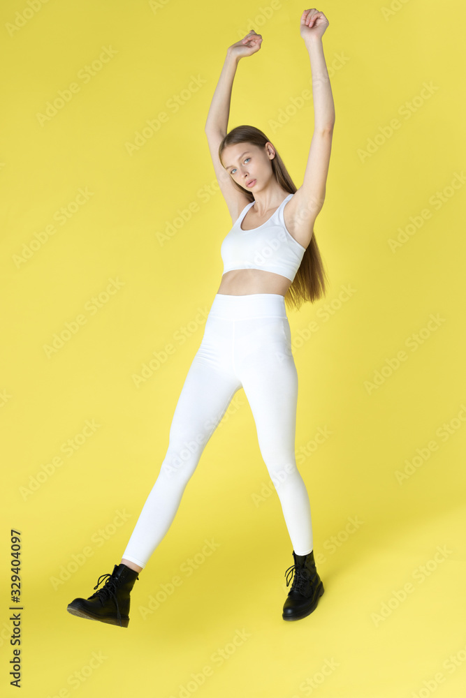 Young woman in white blank leggings and a crop top on a yellow background. Mock-up. Young woman in white blank leggings and a crop top on a yellow background. Mock-up.