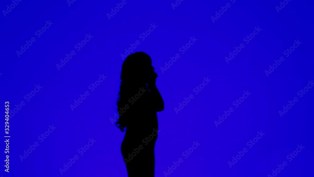 Silhouette of a young woman with curly hair talking on a cell phone on a blue background Silhouette of a young woman with curly hair talking on a cell phone on a blue background