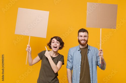 Obraz na plátně Excited protesting two people guy girl pointing index finger on protest signs broadsheet blank placard on stick isolated on yellow background
