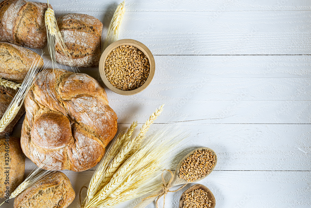 Traditional wheat bread, rolls and ears of cereals on a white wooden background