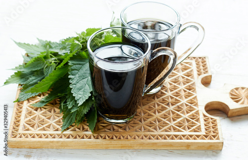 Nettle tea or decoction in glass cups and fresh urtica herb isolated on white wood, first spring vitamin green food and salad ingredient, closeup, copy empty space, healing herb concept