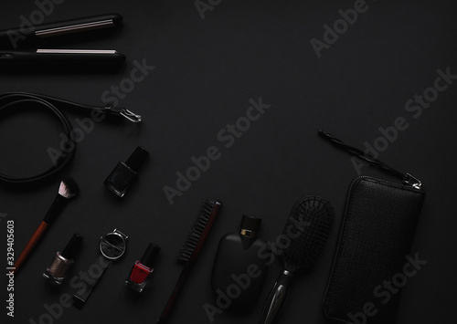 Accessories for women's beauty. Make up brush, watch, nail polish and hair straightener, all on a black background with top view and copy space. Minimalist black trend 2020 and cosmetics background.