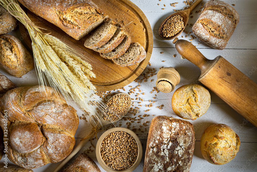 Traditional wheat bread, rolls and ears of cereals on a white wooden background