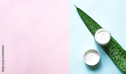 Concept of natural beauty products. With white cream for skin care on a pastel blue background with green leaves. Top view and copy space