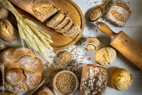 Obraz na płótnie Traditional wheat bread, rolls and ears of cereals on a white wooden background w salonie