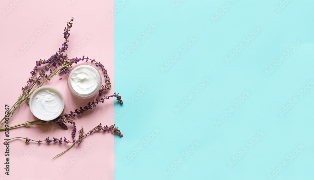 Fototapeta premium Concept of natural beauty products. With white cream and lavender flower for skin care on a pastel blue background with green leaves. Top view and copy space Flat lay.