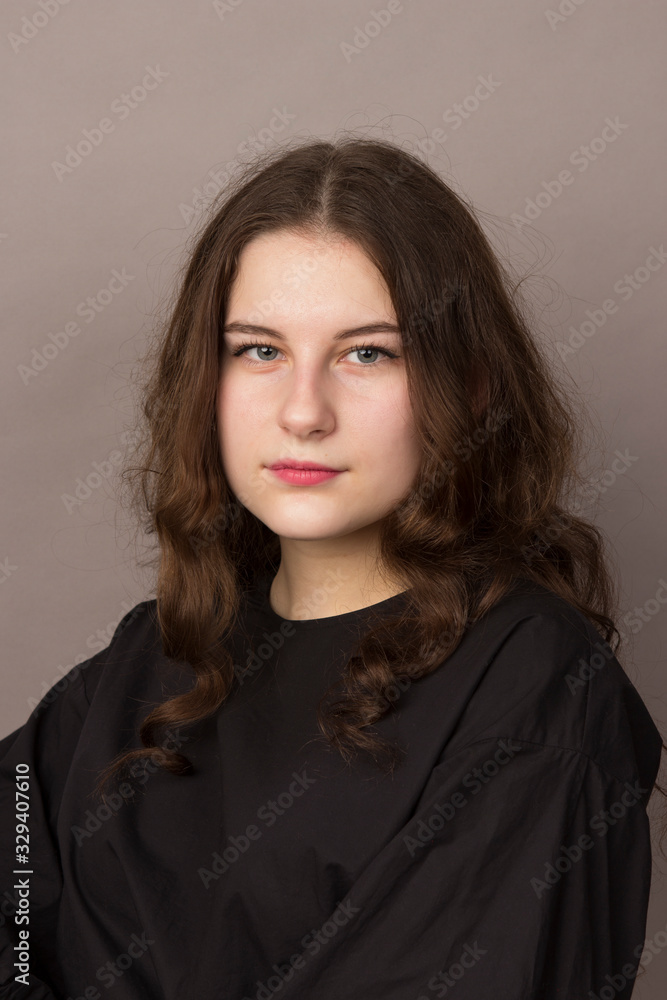 Beautiful brunette young girl with curly wavy brown hair, white skin in black clothes is photographed in the studio against the background of a coffee wall. Beautiful brunette young girl with curly wavy brown hair, white skin in black clothes is photographed in the studio against the background of a coffee wall.