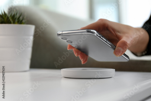 Woman putting smartphone on wireless charger in room, closeup photo