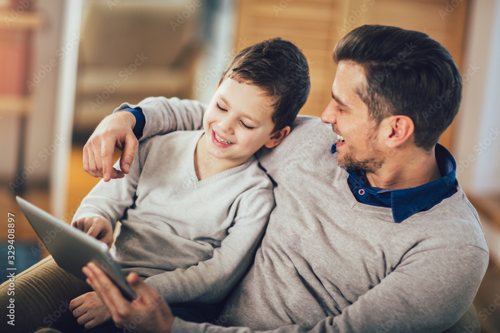 Father and son playing on a tablet at home, having fun Father and son playing on a tablet at home, having fun