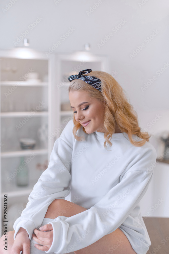 Sexy  blonde in white sweatshirt and knee socks posing at the kitchen table