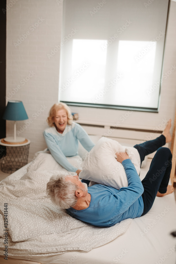 Laughing elderly couple having pillow fight on bed at their home. Laughing elderly couple having pillow fight on bed at their home.