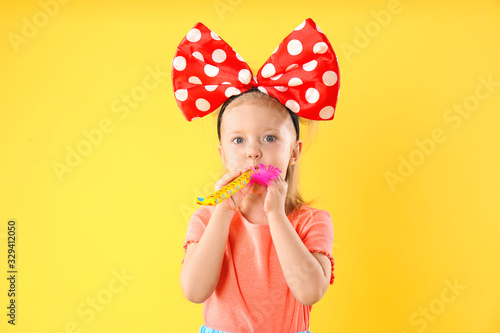 Little girl with large bow and party horn on yellow background. April fool's day