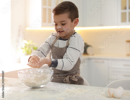 Cute little boy cooking dough at table in kitchen