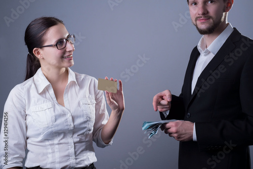 two young business people.A smiling girl is holding a plastic card in her hand, looking at the guy who is pointing at the camera while pointing to the press of cash dollar bills in his hand photo