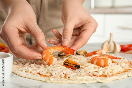 Woman adding shrimp to seafood pizza at white marble table, closeup