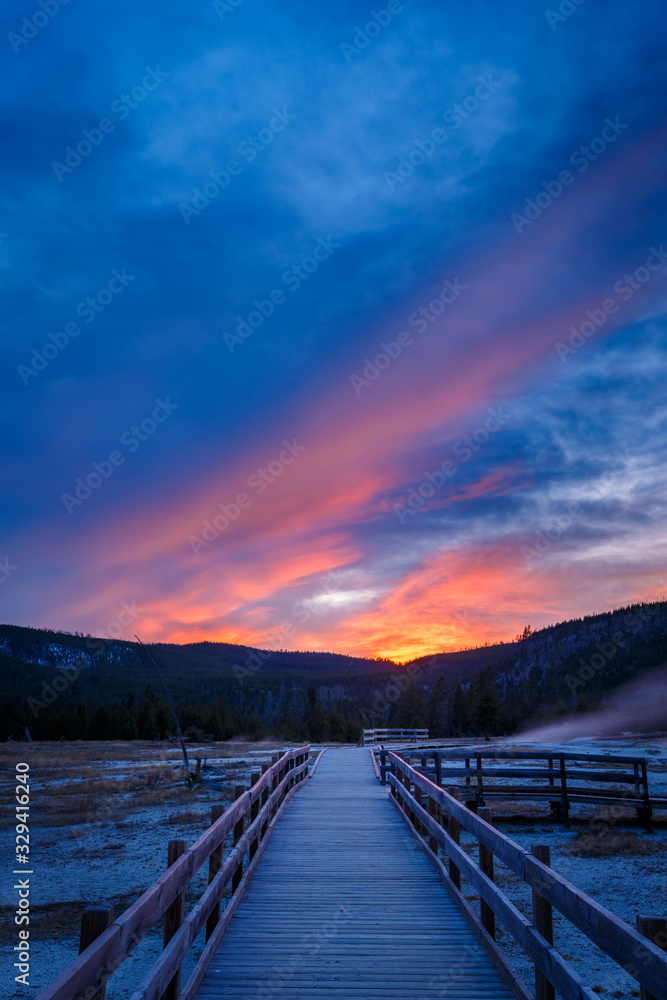 Naklejka premium Biscuit basin walkway with blue steamy water and beautiful colorful sunset. Yellowstone, Wyoming, USA