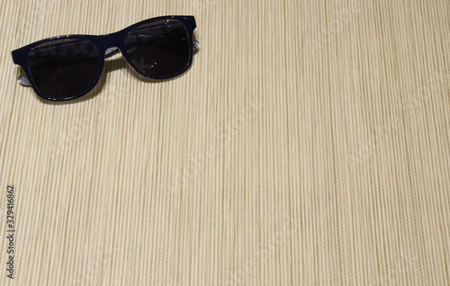 dark sunglasses lie on the background, material from straw of light beige color. Horizontal lines, texture. Relaxation
