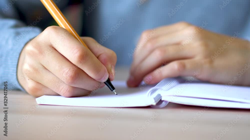 On a light table lies an open notebook on a spring. Yellow pen on a notebook. The girl takes a pen and makes an entry in a notebook. Close up view. On a light table lies an open notebook on a spring. Yellow pen on a notebook. The girl takes a pen and makes an entry in a notebook. Close up view.
