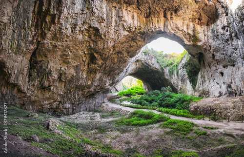 Devetashka cave interior, near Lovech town, Bulgaria. Panorama of entrance tunnel with hole on top and deep green grass