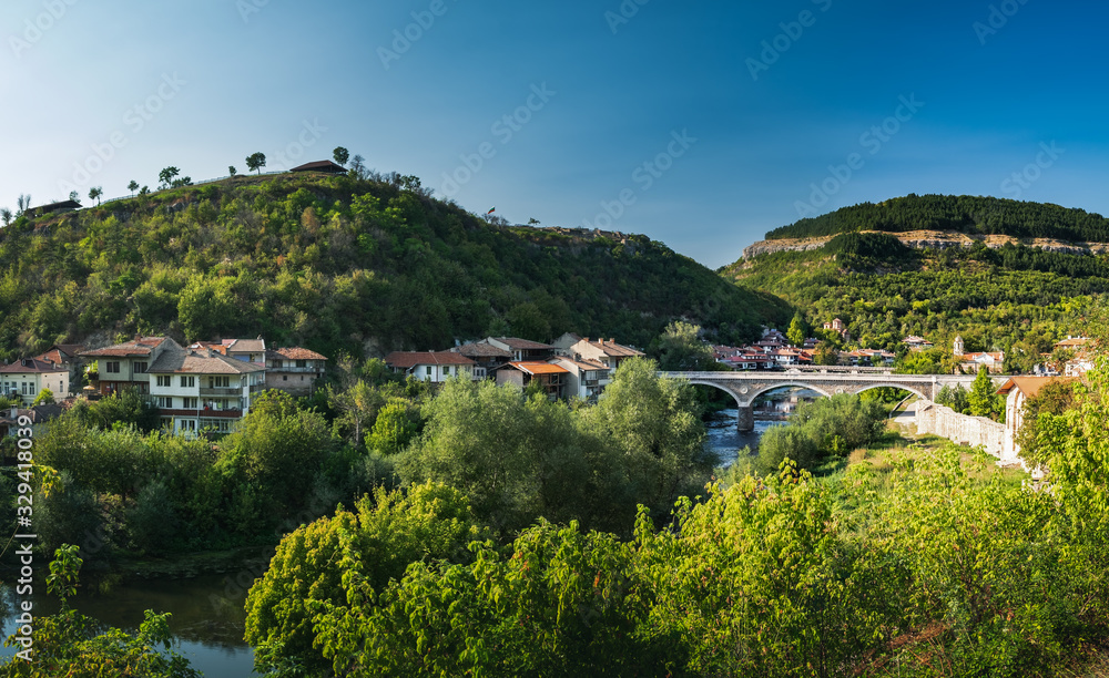 Panoramic view of Veliko Tarnovo from Tsarevets hill in summer. Typical Bulgarian town in Eastern Europe, river landscape, bridge and terrace architecture in Veliko Tarnovo, Bulgaria. Panoramic view of Veliko Tarnovo from Tsarevets hill in summer. Typical Bulgarian town in Eastern Europe, river landscape, bridge and terrace architecture in Veliko Tarnovo, Bulgaria.