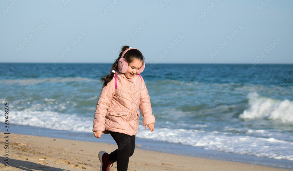 little girl in earmuffs and jacket run along the beach
