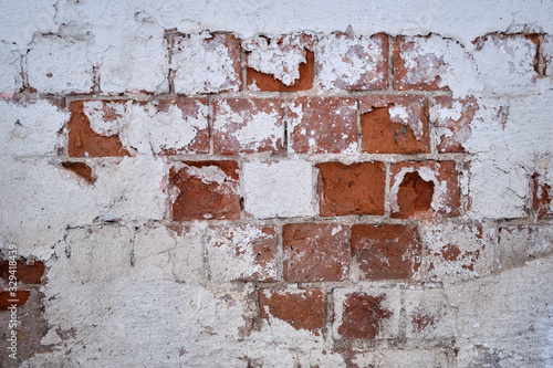 Background. An old red brick wall with peeled white paint and peeled plaster.