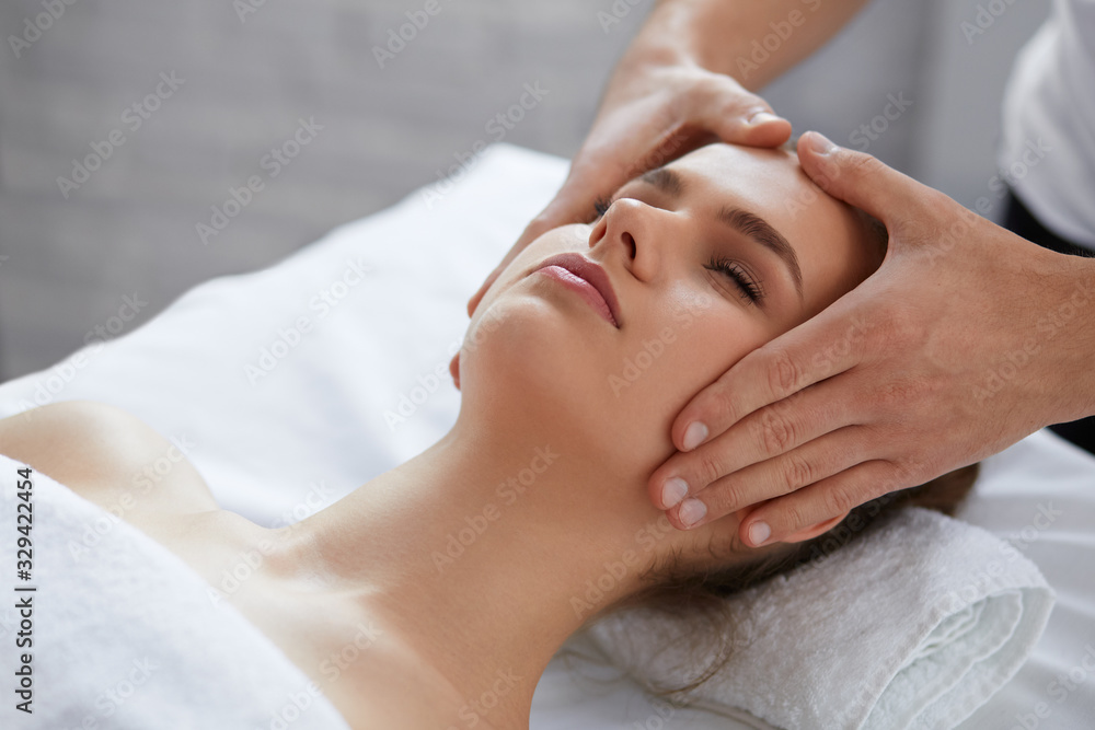 Young beautiful woman enjoying anti-aging facial massage.Male therapist making head massage to female client.Professional masseur.Relaxation,beauty,spa,body and face treatment concept.