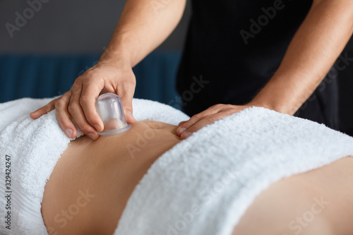 Young beautiful woman enjoying cupping massage in spa.Professional massage therapist is treating a female patient in apartment.Relaxation beauty body and face treatment concept.Home massage.
