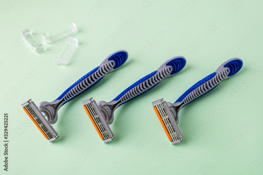 Three new disposable shaving razors with triple blade lie in a row on a pastel green background