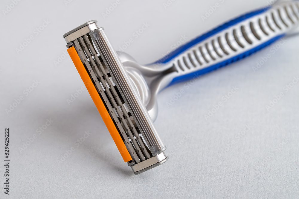 Close-up of new disposable shaving razor with triple blade on a pastel gray background. Silver blue plastic razor with orange lubricat strip. Personal hygiene accessory. Close-up of new disposable shaving razor with triple blade on a pastel gray background. Silver blue plastic razor with orange lubricat strip. Personal hygiene accessory.