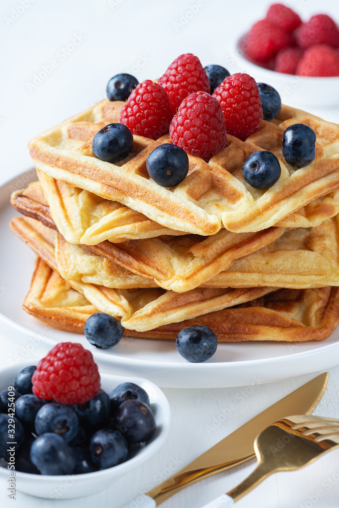 Homemade waffles with raspberries and blueberries in a plate on a white table Homemade waffles with raspberries and blueberries in a plate on a white table