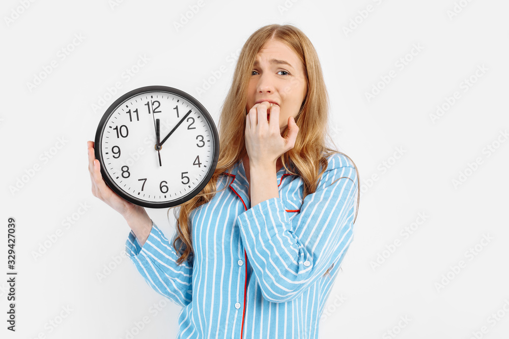 Frightened sleepy girl in pajamas holding an alarm clock on a white background Frightened sleepy girl in pajamas holding an alarm clock on a white background