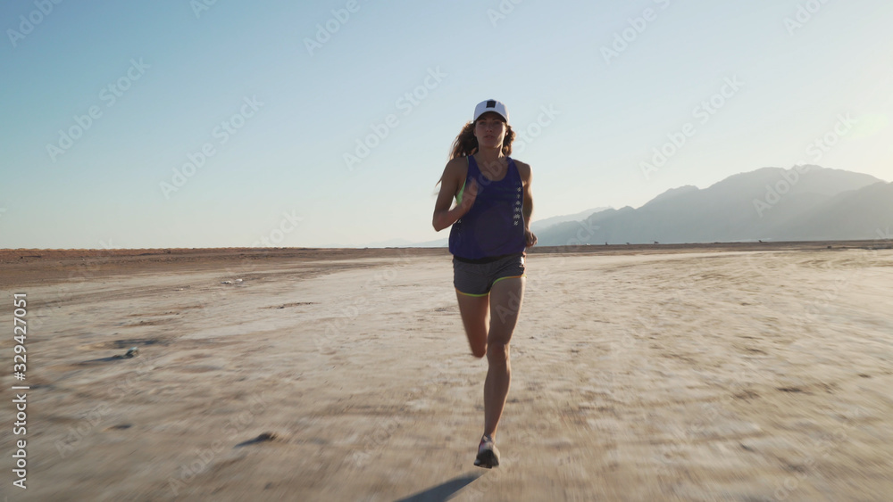 Young fit caucasian girl jogging in dry desert at sunrise.