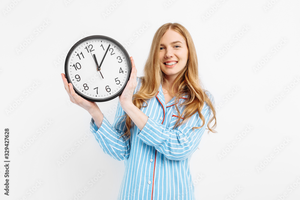 Happy girl dressed in her pajamas, holding the watch rejoices on a white background Happy girl dressed in her pajamas, holding the watch rejoices on a white background